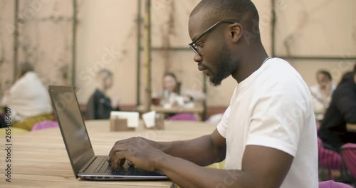 Persistent afroamerican student dressed in white t-shirt working on laptop sitting in outdoors cafe