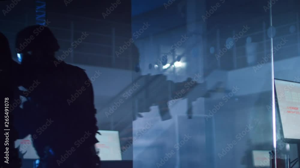 Masked Squad of Armed SWAT Police Officers Storm a Dark Seized Office Building with Desks and Computers. Soldier Breaks a Glass with His Arm and Team Continue to Move. Warm Color Grade. Masked Squad of Armed SWAT Police Officers Storm a Dark Seized Office Building with Desks and Computers. Soldier Breaks a Glass with His Arm and Team Continue to Move. Warm Color Grade.