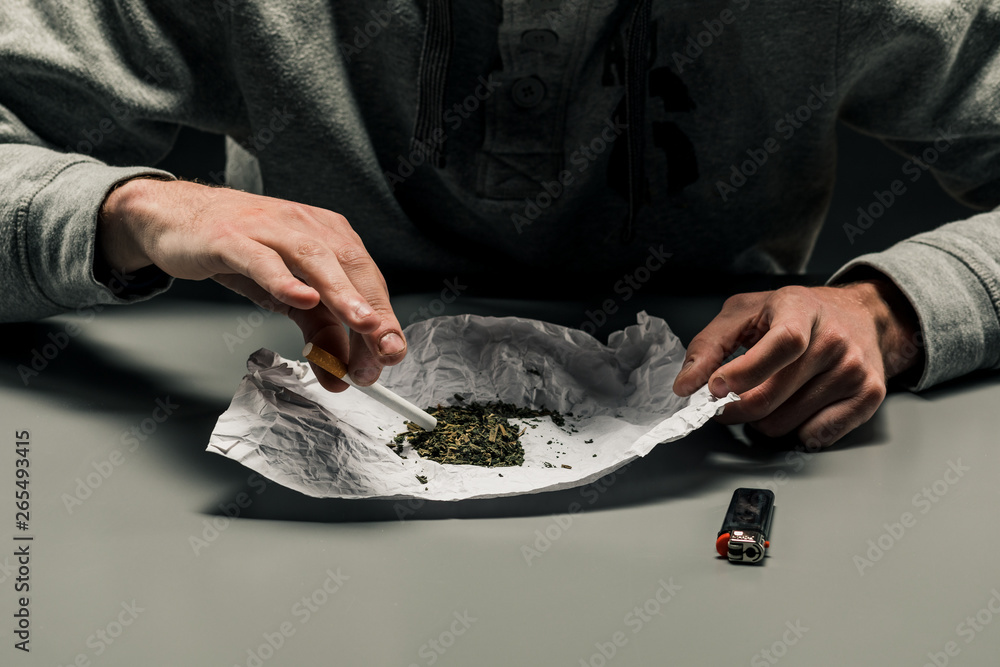A drug addict makes a cigarette with marijuana. The concept of drug abuse and traffic.