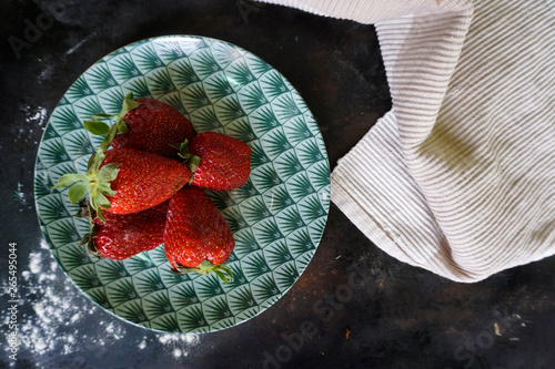 Group of strawberries on green pattern ceramic plate and white linene napkin on dark background. photo