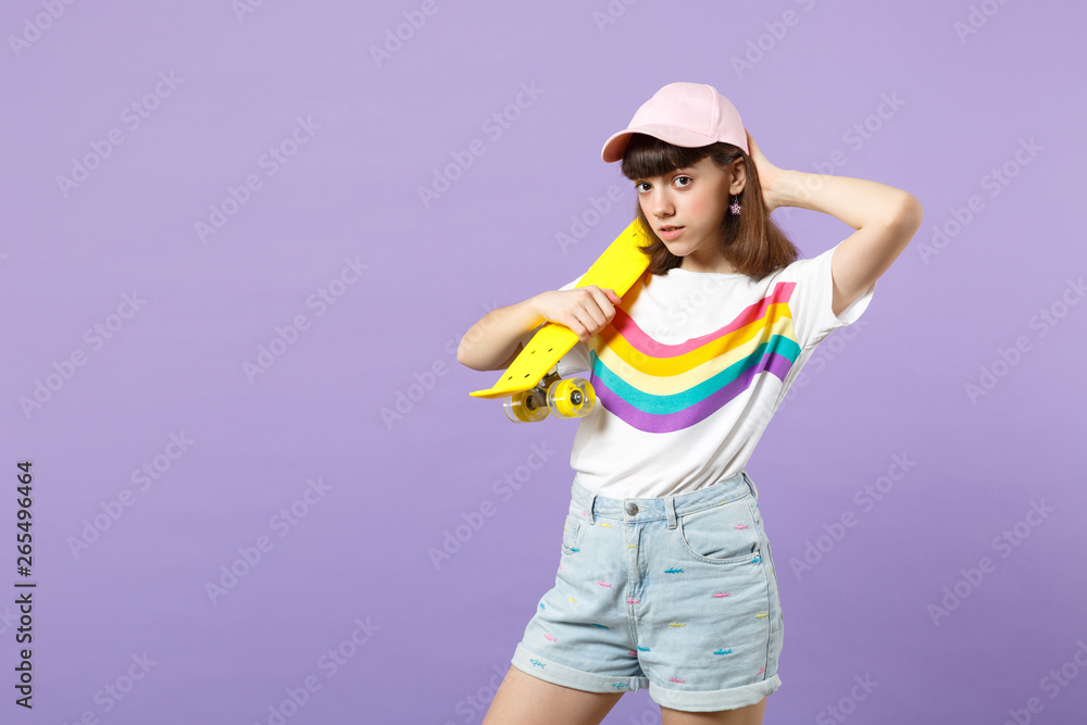 Portrait of beautiful teen girl in vivid clothes looking camera holding yellow skateboard isolated on violet pastel background in studio. People sincere emotions lifestyle concept. Mock up copy space. Portrait of beautiful teen girl in vivid clothes looking camera holding yellow skateboard isolated on violet pastel background in studio. People sincere emotions lifestyle concept. Mock up copy space.