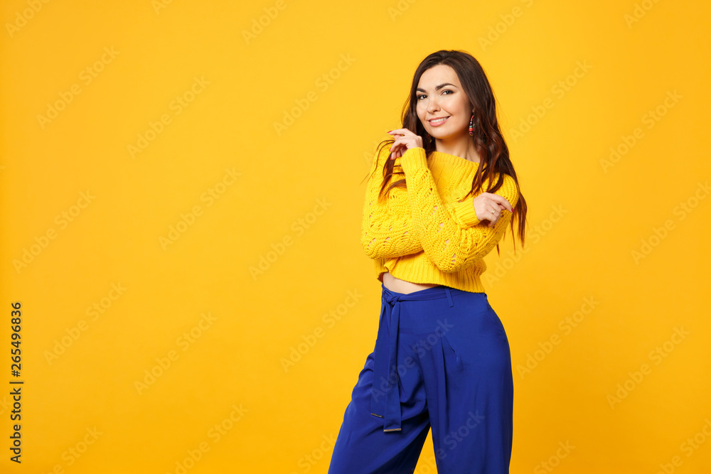 Smiling young woman in sweater, blue trousers looking camera, holding hands crossed isolated on yellow orange wall background in studio. People sincere emotions, lifestyle concept. Mock up copy space. Smiling young woman in sweater, blue trousers looking camera, holding hands crossed isolated on yellow orange wall background in studio. People sincere emotions, lifestyle concept. Mock up copy space.