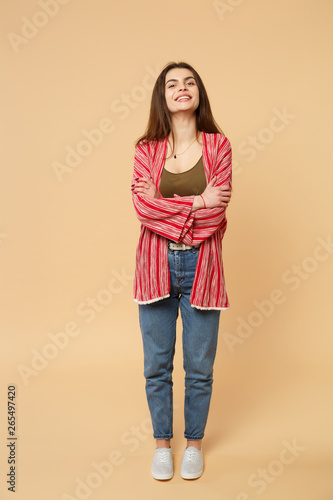 Portrait of joyful young woman in casual clothes looking camera, holding hands crossed isolated on pastel beige background in studio. People sincere emotions, lifestyle concept. Mock up copy space.