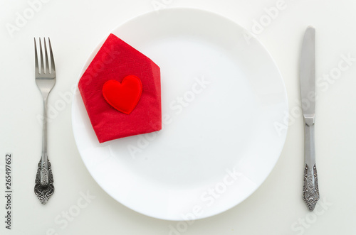 Flat lay romantic dinner proposal concept. Dish with cutlery and heart on a red napkin with with background