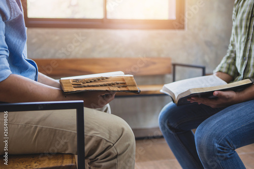 Fotografie Two young man sitting on wooden chair while read holy bible together