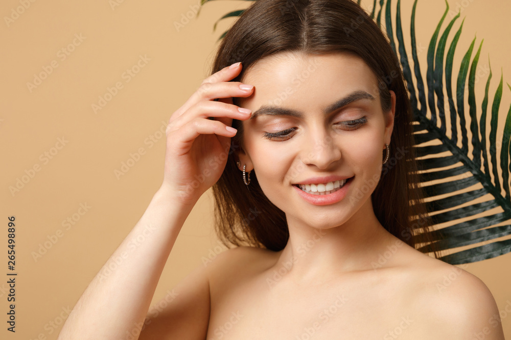 Close up brunette half naked woman 20s with perfect skin, nude make up palm leaf isolated on beige pastel wall background, studio portrait. Health care cosmetic procedures concept. Mock up copy space. Close up brunette half naked woman 20s with perfect skin, nude make up palm leaf isolated on beige pastel wall background, studio portrait. Health care cosmetic procedures concept. Mock up copy space.