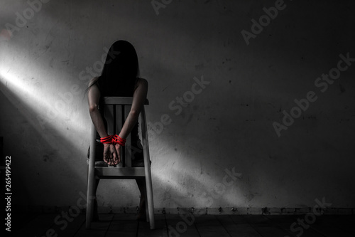 Young woman sitting on chair and  tied up with rope ,Victim woman tied with red rope sit on chair in abandon house,Sexual abuse or rape in dirty room with copy space,mono tone .