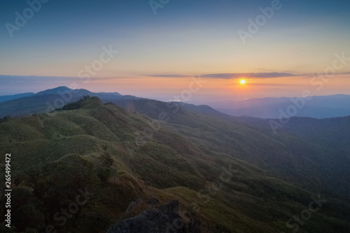 Mountain view morning above many hills and green forest around with soft fog with colorful red sun light in the sky background, sunrise at top of Phu Langka Forest Park, Phayao, Thailand.