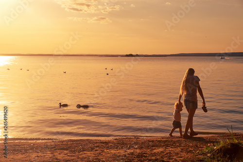 Young mother plays with her child in the summer near the lake at sunset in the evening © khmelev