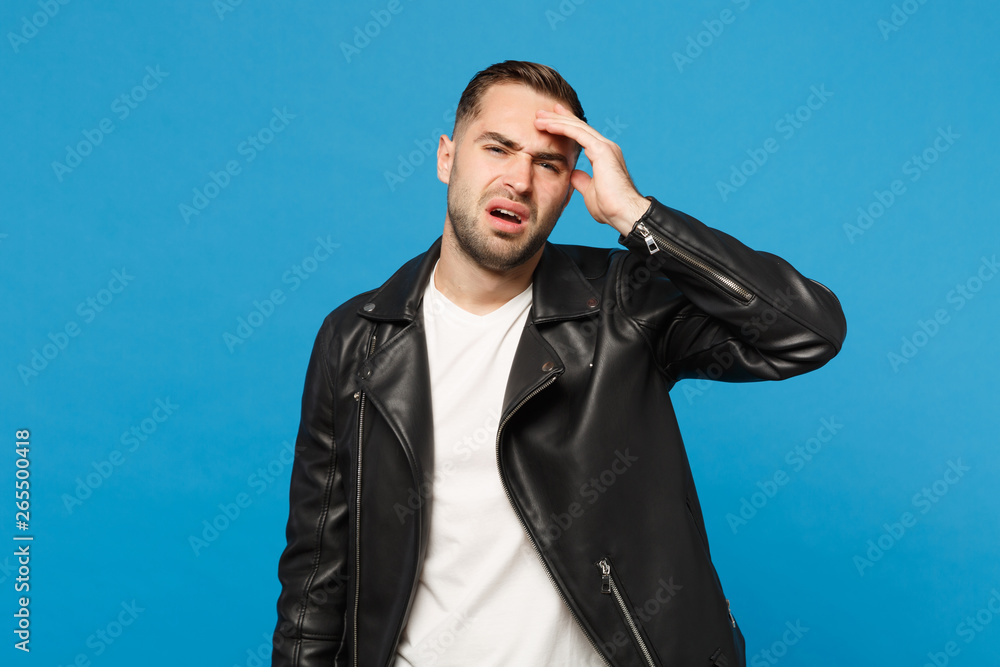 Young sad frustrated worried unshaven man in black jacket white t-shirt looking camera isolated on blue wall background studio portrait. People sincere emotions lifestyle concept. Mock up copy space. Young sad frustrated worried unshaven man in black jacket white t-shirt looking camera isolated on blue wall background studio portrait. People sincere emotions lifestyle concept. Mock up copy space.