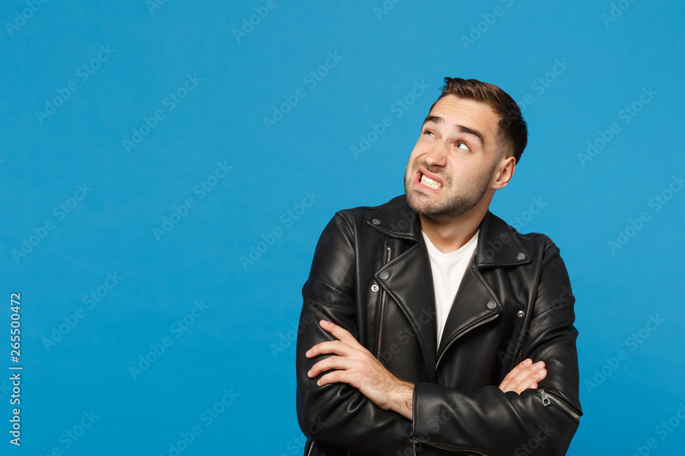 Young sad frustrated worried unshaven man in black jacket white t-shirt looking aside isolated on blue wall background studio portrait. People sincere emotions lifestyle concept. Mock up copy space. Young sad frustrated worried unshaven man in black jacket white t-shirt looking aside isolated on blue wall background studio portrait. People sincere emotions lifestyle concept. Mock up copy space.