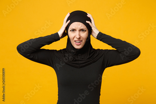 Sad upset crying confused young arabian muslim woman in hijab black clothes posing isolated on yellow wall background, studio portrait. People religious Islam lifestyle concept. Mock up copy space. © ViDi Studio