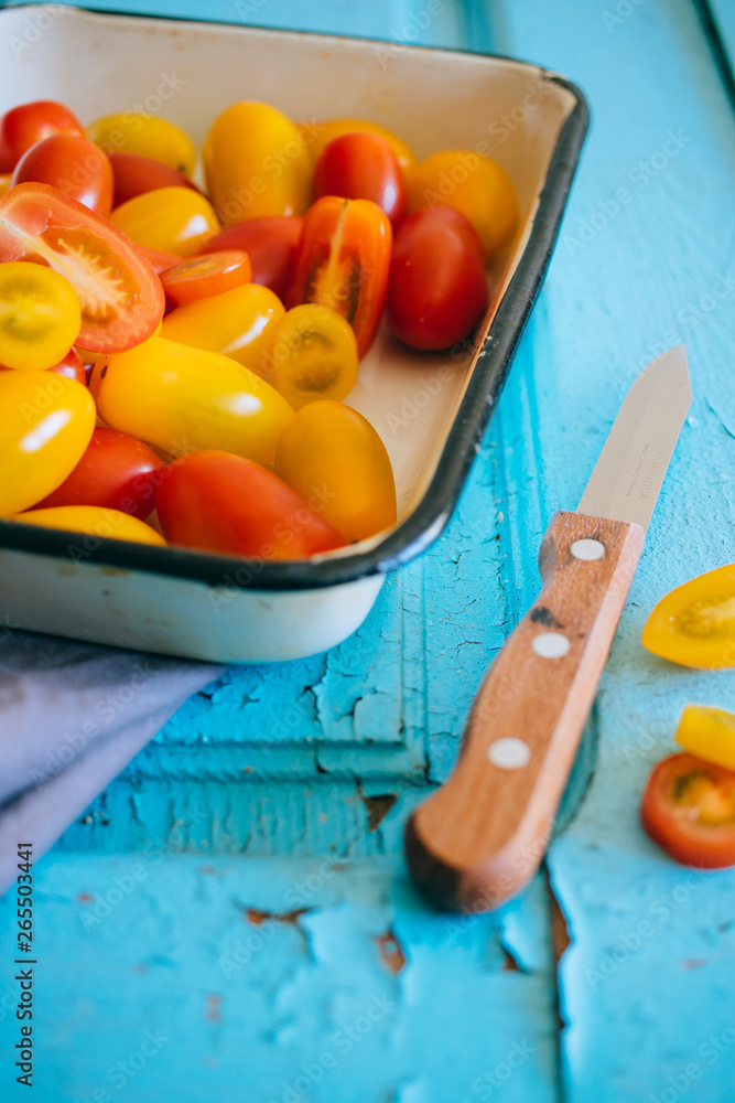 Small cherry tomatoes, red and yellow, in an enameled baking sheet on a blue background