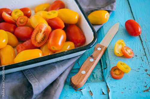 Small cherry tomatoes  red and yellow  in an enameled baking sheet on a blue background