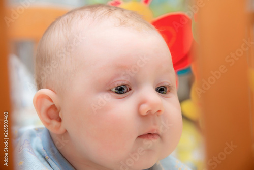 A newborn baby is lying in a children's bed on the background of toys and smiling, close-up.