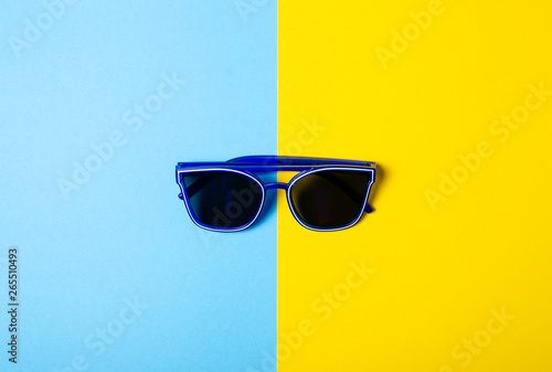 Blue sunglasses fashion on color blue yellow background, top view