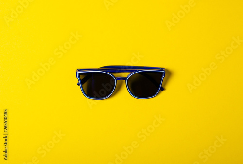 Blue sunglasses fashion on color yellow background, top view