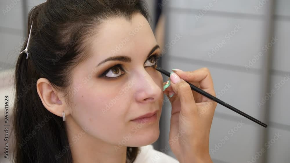 Hands make-up artist applied makeup on the face of a young woman. Girl doing eye makeup in a professional salon. Evening makeup. Smokey eyes. 4k Hands make-up artist applied makeup on the face of a young woman. Girl doing eye makeup in a professional salon. Evening makeup. Smokey eyes. 4k