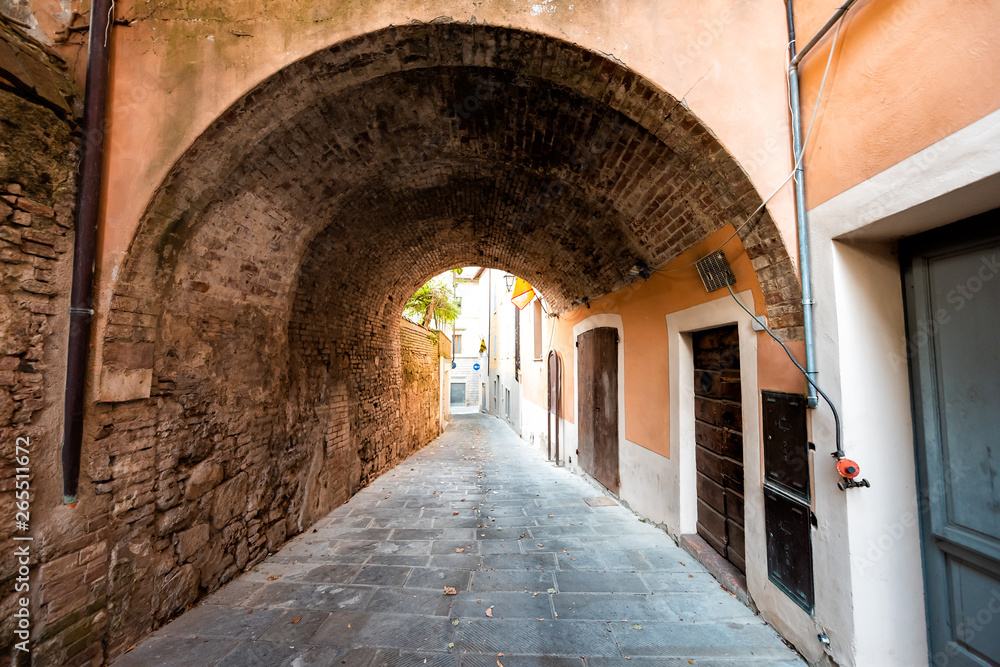 Chiusi, Italy street in small historic medieval town village in Umbria during sunny day with nobody orange yellow pink colorful walls and arch