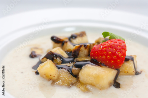 milk porridge with bananas, strawberries, chocolate sauce and mint in a white plate close-up