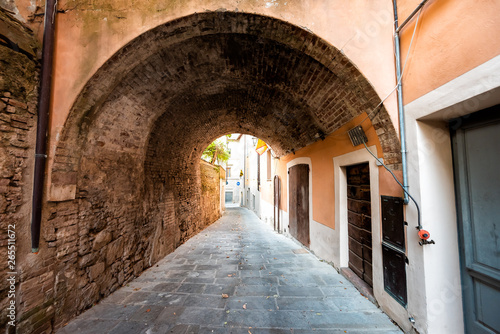 Chiusi, Italy street in small historic medieval town village in Umbria during sunny day with nobody orange yellow pink colorful walls and arch