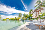Luxury swimming pool in the tropical hotel or resort. Palm trees and infinity pool close to lounge chairs and umbrellas. Exotic travel destination, summer mood, beach holiday