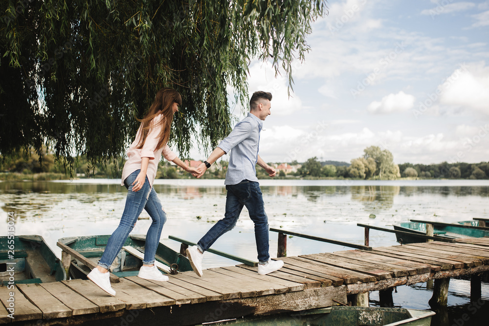  Happy young couple outdoors. young love couple running along a wooden bridge holding hands. love story at the lake