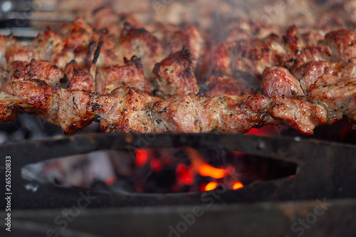 Traditional Caucasian BBQ shashlik grilled meat on sticks being cooked on open fire with smoke, close up view