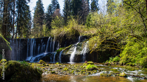 A mystic waterfall hidden in a forest. The water is flowing over a old wall.