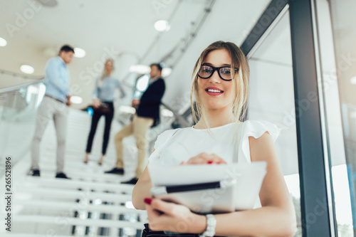 Beautiful business woman girl holding a tablet in her hands and smiling at the camera. In the background are business people.