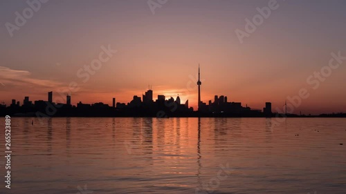 Toronto Skyline Sunrise Time lapse. Sun rises behind the CN Tower and Downtown Area of Big Canadian City in Ontario. Colorful Blue, Golden and Pink Sky Transformation. Reflections Can be Seen on Water