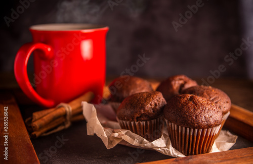 Fresh chocolate muffins and cinnamon sticks on rustic wooden background