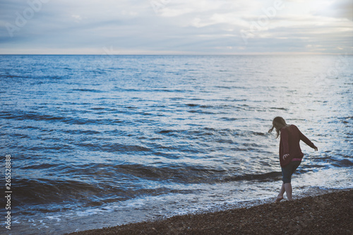 A woman walking by the shoreline dipping her toe in the sea in the evening