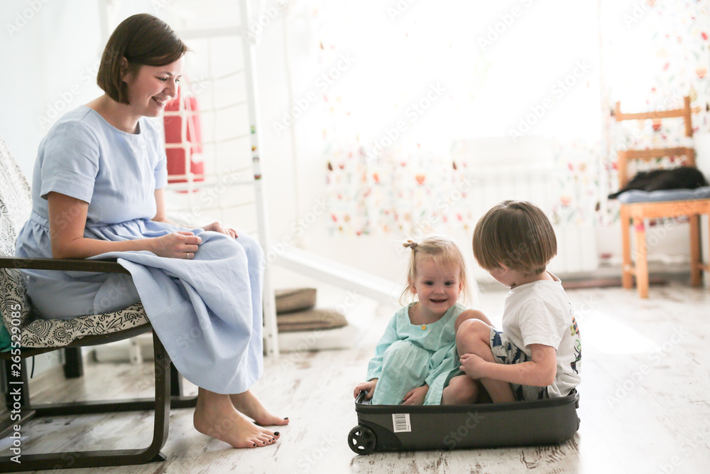 Children are sitting in suitcase near mother Children are sitting in suitcase near mother