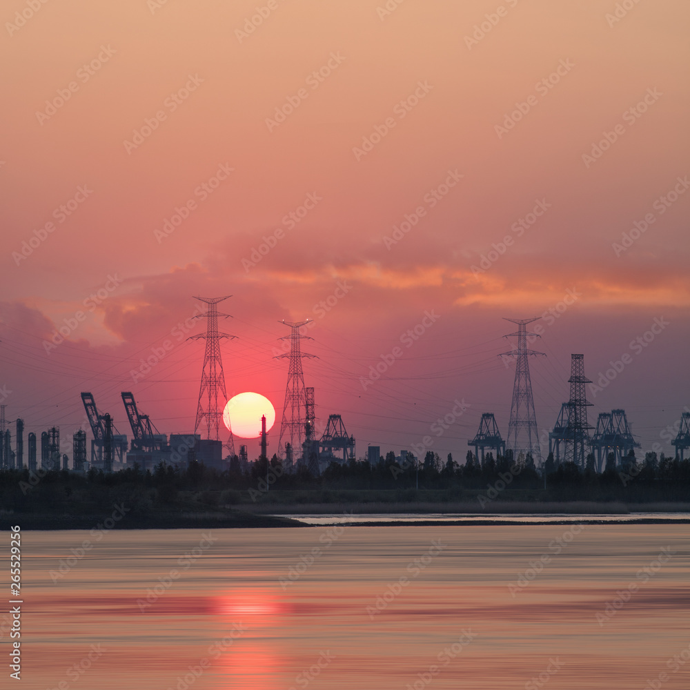 Riverbank with silhouettes of container terminal cranes during a red colored sunset, Port of Antwerp, Belgium.