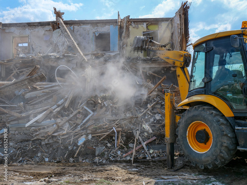Destruction of walls of old building and cleaning of construction debris with bucket of excavator..bulldozer demolishing concrete brick walls of small building