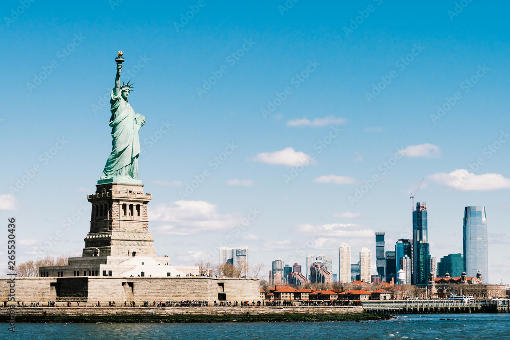 Statue of Liberty on sunny day with New York city Manhattan island in background. America cityscape, United States nation symbol, travel destination or tourist attraction concept Statue of Liberty on sunny day with New York city Manhattan island in background. America cityscape, United States nation symbol, travel destination or tourist attraction concept