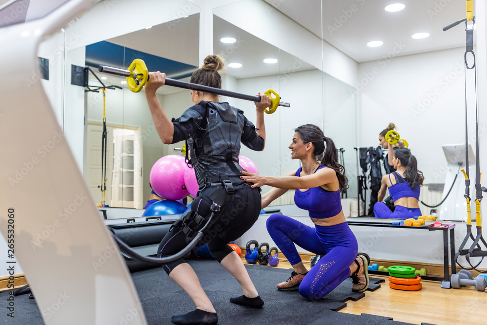 Athletic woman during functional workout with electric muscle stimulation  in fitness gym. EMS electro stimulation women exercises with trainer coach  Stock Photo