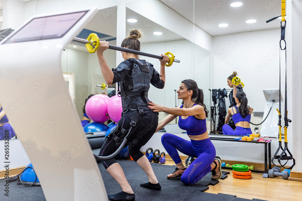 EMS electro stimulation women exercises with trainer coach. Female athlete wearing ems workout