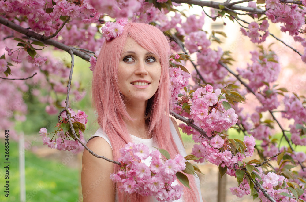 Beautiful girl in cherry blossom garden on a spring day. Woman with pink hair Beautiful girl in cherry blossom garden on a spring day. Woman with pink hair