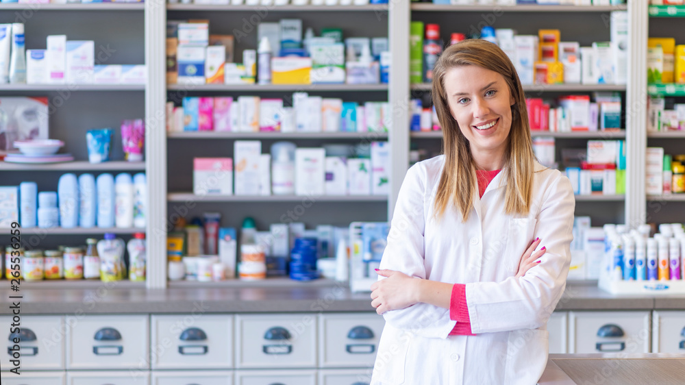 Portrait of a smiling pharmacist with arms crossed at modern pharmacy. Beautiful woman wearing in white lab coat working in drugstore. Portrait of a smiling pharmacist with arms crossed at modern pharmacy. Beautiful woman wearing in white lab coat working in drugstore.