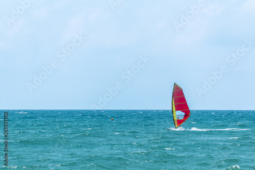 Summer Windsurfing. Male sportsman standing on a sailboard and gliding along the sea waves on a seascape background.
