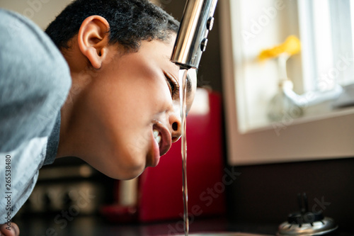 child afro american boy take water on his mouth and drink in a kitchen.
