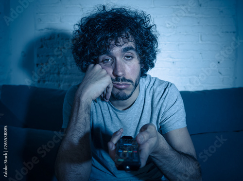 Portrait of bored sleepless young man sitting on the couch watching TV at night photo