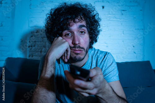 Fotografie Portrait of bored sleepless young man sitting on the couch watching TV at night