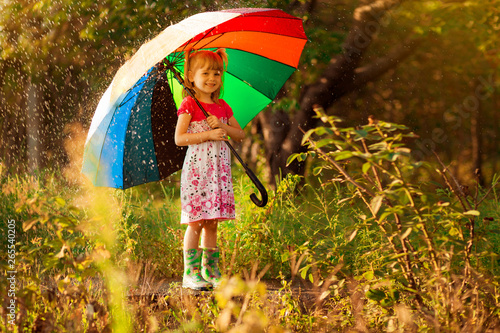 Happy child girl walk with multicolored umbrella under rain