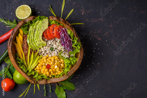 Buddha bowl with chickpea, avocado, wild rice, quinoa seeds, bell pepper, tomatoes, greens, cabbage, lettuce on shabby dark stone table. Vegetarian super food. Top view with copy space.