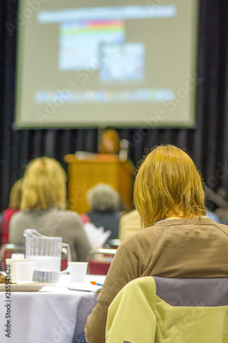 Woman watching keynote speaker at a conference with a slide deck presentation projected