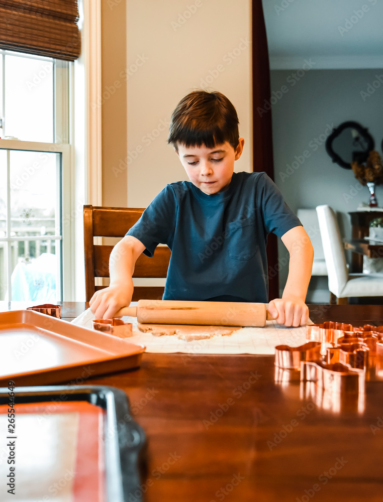 Young boy rolling out cookie dough with rolling pin at the table. Young boy rolling out cookie dough with rolling pin at the table.