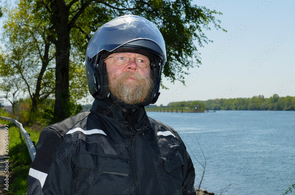 Mann mit langem Bart, Brille und Motorradhelm, steht am Ufer des Rhein Mann mit langem Bart, Brille und Motorradhelm, steht am Ufer des Rhein